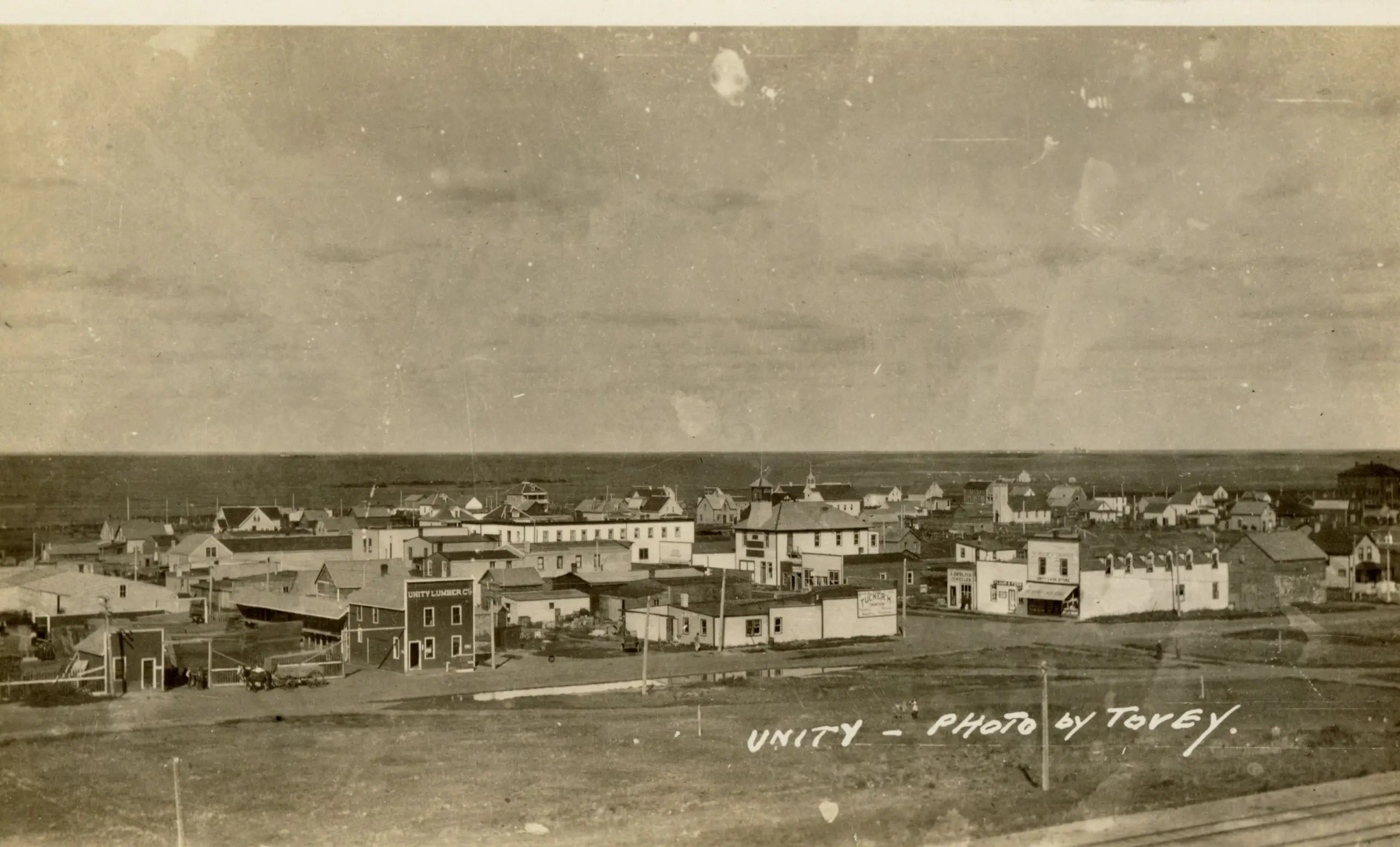 Overview of Unity from a rise, with lumber company and main street buildings