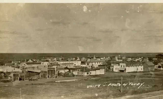 Overview of Unity from a rise, with lumber company and main street buildings